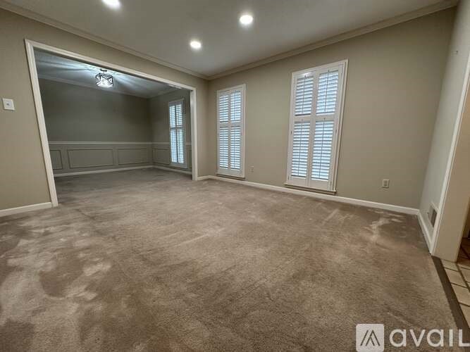 A spacious room with carpeted floor and a large window with blinds.