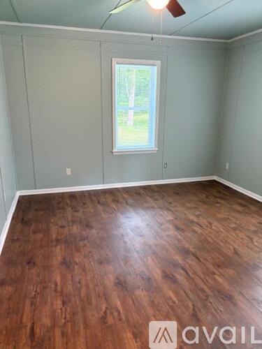 A room with wooden flooring and a window showing greenery outside.