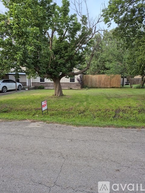 A tree in a yard with a sign that says "For Sale".