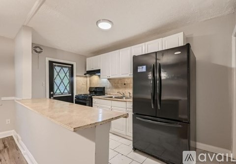 A black refrigerator in a kitchen with white cabinets.