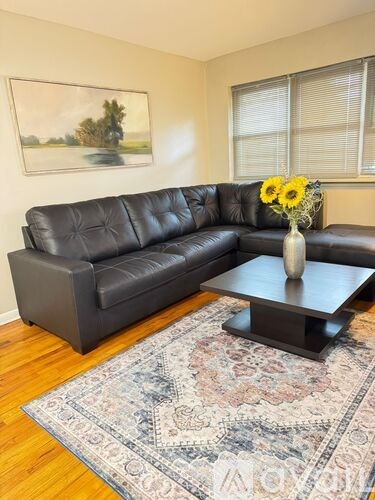 A black leather sofa with a vase of yellow flowers on a coffee table in a room with a painting on the wall.