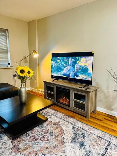 A television is on a stand with a vase of flowers and a lit lamp.