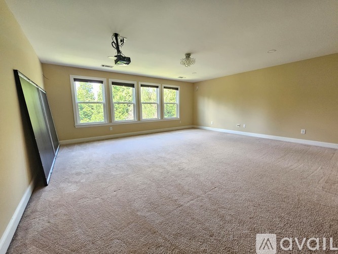 A spacious room with carpeted floor, a flat-screen TV, and large windows.