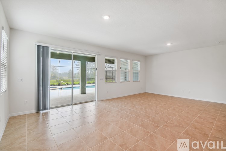 A spacious room with tiled flooring and a sliding glass door leading to a pool area.