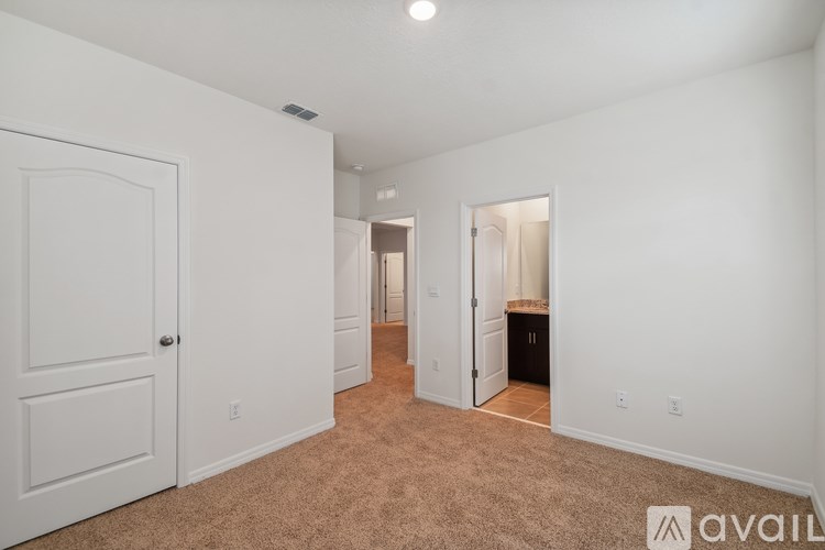 A room with white walls and carpeted floor with a door on the left and a bathroom visible through an open door on the right.