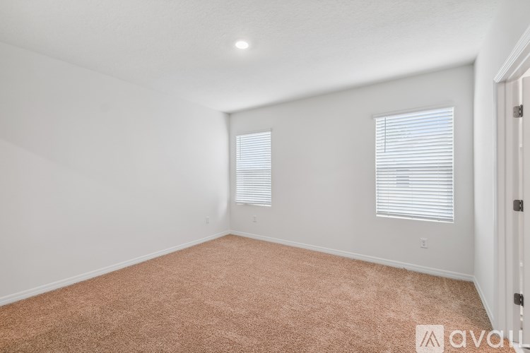 A room with carpeted floor and two windows with blinds.