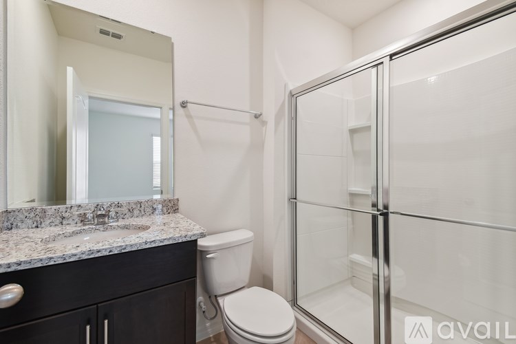 A bathroom with a toilet, sink, mirror, and shower.