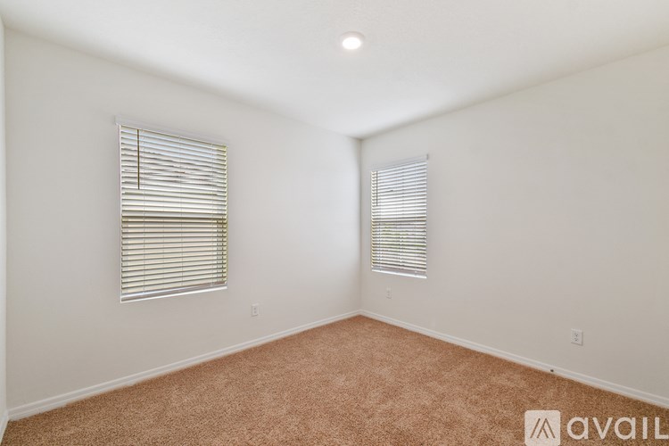 A room with carpeted floor and two windows with blinds.