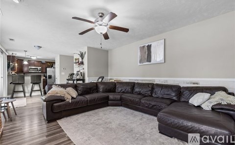 A living room with a black leather couch and a ceiling fan.