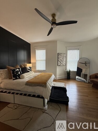 A bedroom with a bed, a fan, and a chair.