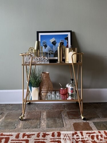 A gold bar cart with a framed picture on top and a vase with a plant on it.