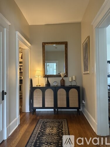 A hallway with a mirror, lamp, and a cabinet with a screen door.
