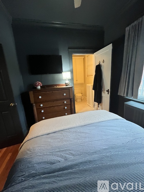A bed with a striped comforter sits in a bedroom with a dresser and a doorway leading to a bathroom.