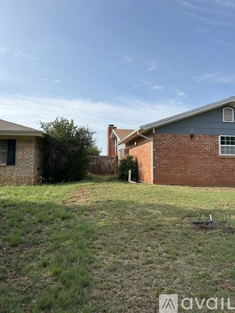 A grassy area with a house and a tree in the background.