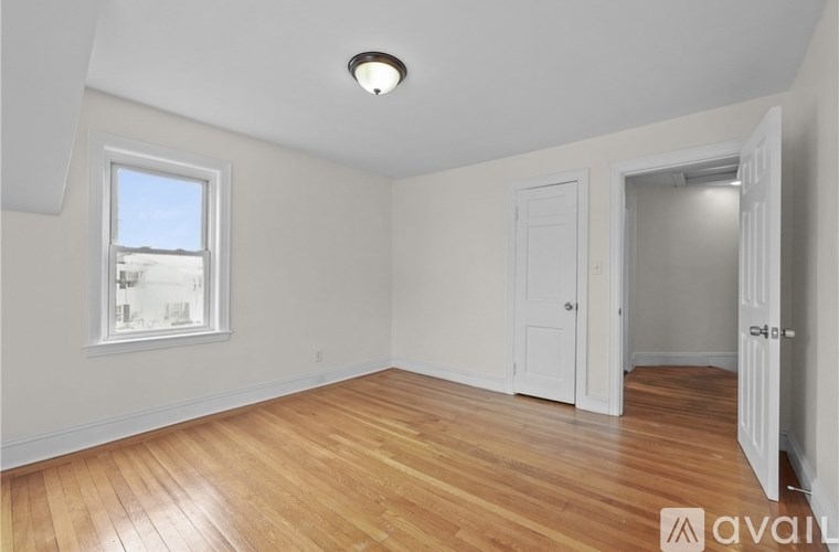 A room with wooden floors and white walls, with a window and a door.