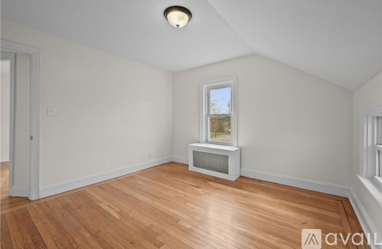 A room with wooden floors and a window with a white air conditioning unit under it.