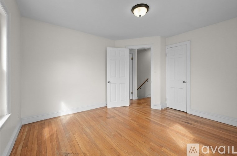 A room with wooden floors and white walls, with a doorway leading to another room.