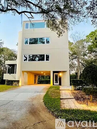 A modern house with a flat roof and large windows is surrounded by greenery.
