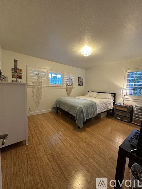 A bedroom with a bed, nightstand, and a window with blinds.