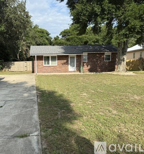 A small brick house with a white door and a window is surrounded by a grassy area and trees.