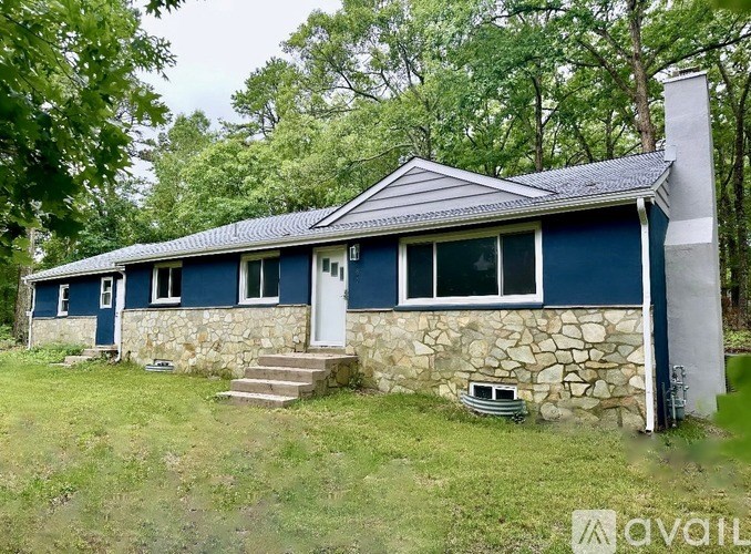 A blue house with a white door and windows is surrounded by greenery.