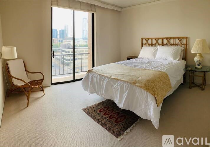 A bedroom with a large bed, a chair, and a view of the city.
