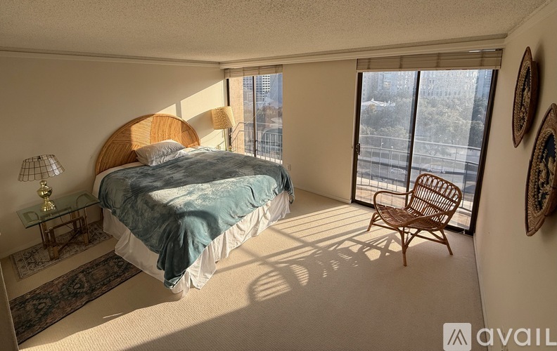 A bedroom with a large bed and a view of the city through the sliding glass door.