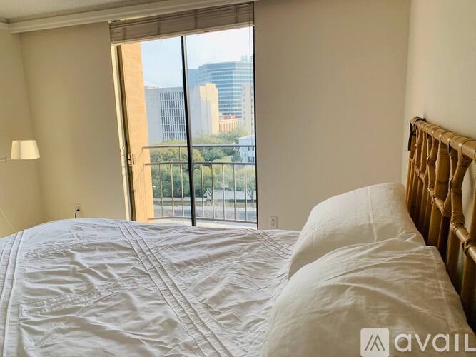 A bedroom with a large bed and a view of the city through the sliding glass door.