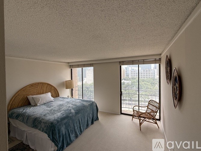 A bedroom with a bed, chair, and window overlooking a cityscape.