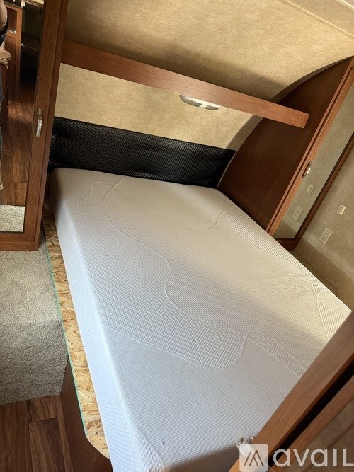 A bed with a white mattress is seen in a room with wooden flooring and a beige wall.