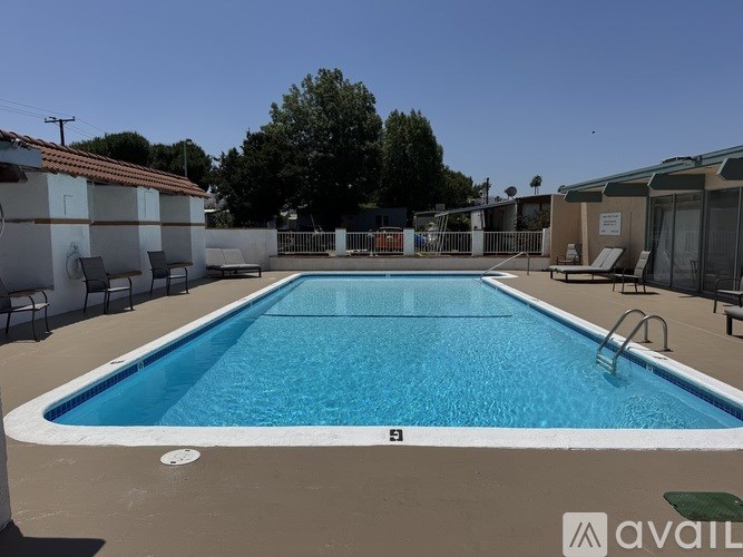 A large outdoor swimming pool surrounded by chairs and a clear blue sky.