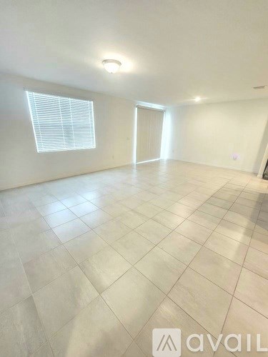 A spacious room with tiled flooring and a window with blinds.