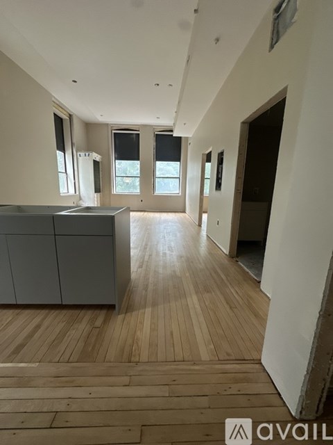 A spacious room with wooden flooring and a kitchen area with a refrigerator, sink, and cabinets.