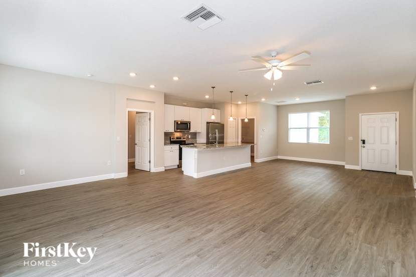 A spacious living room with a kitchen in the background and a ceiling fan above.