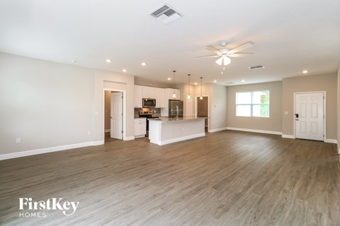 A spacious living room with a kitchen in the background and a ceiling fan above.