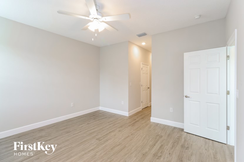 A spacious room with a ceiling fan and light fixture, and a door on the right.