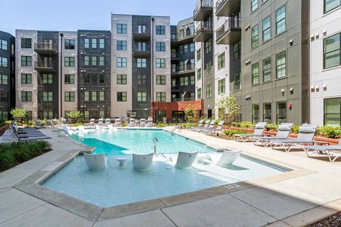 A swimming pool surrounded by lounge chairs in front of apartment buildings.