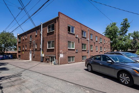 A grey car is parked in front of a red brick building.