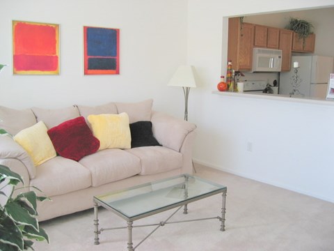 A living room with a couch, a glass table, and two paintings on the wall.