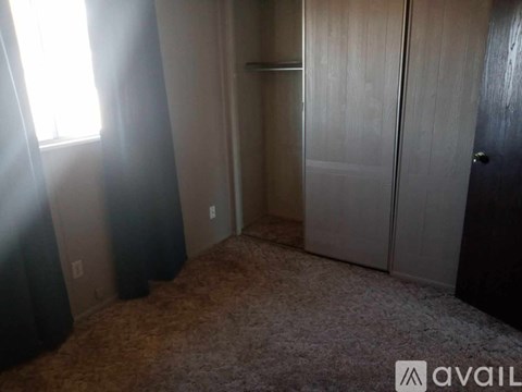 A room with a carpeted floor, a door, and a window with curtains.