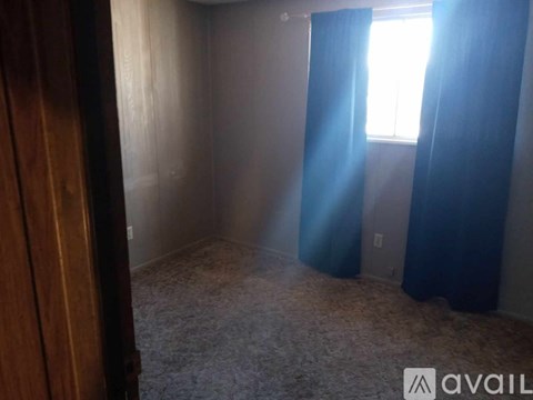A room with a carpeted floor and a window with blue curtains.