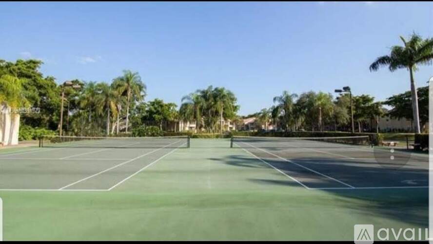 A tennis court surrounded by palm trees under a clear blue sky.