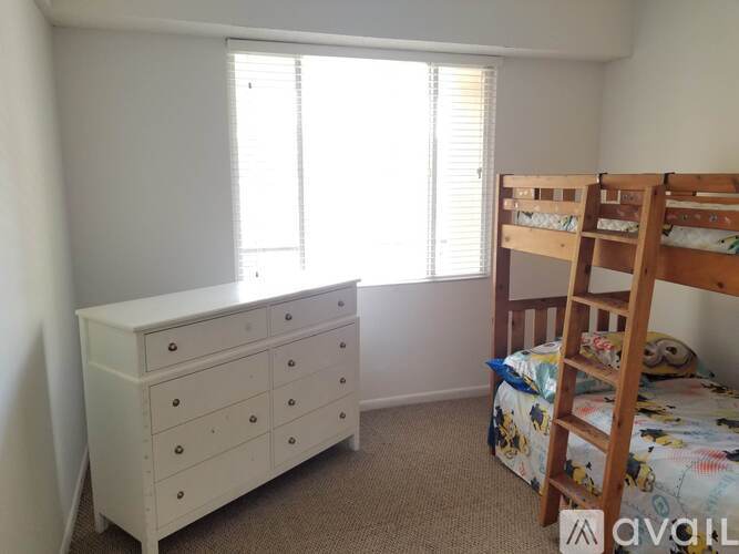 A white dresser sits next to a bunk bed in a room with a window.