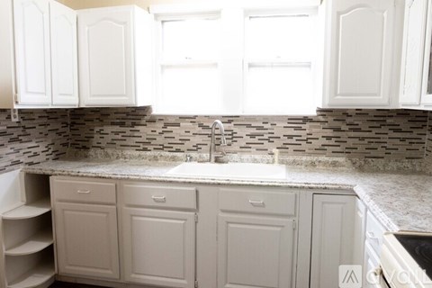 A kitchen with white cabinets and a stone backsplash.