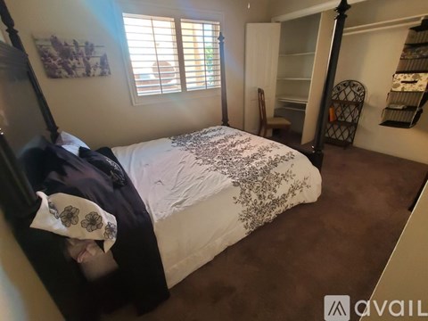 A bedroom with a bed, a chair, and a window with blinds.
