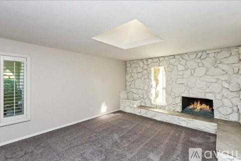 A living room with a stone fireplace and a grey carpet.
