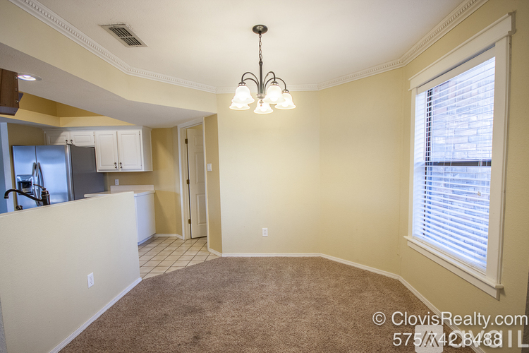 A well-lit, empty room with a carpeted floor and a window with blinds.