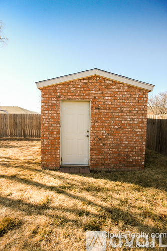 A small brick building with a white door is situated in a grassy area.