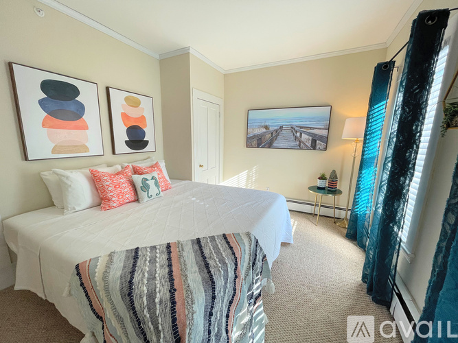 A bedroom with a bed, two pillows, a blanket, a painting, and a window with curtains.