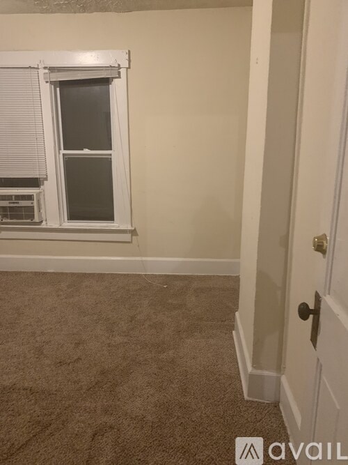 A room with a carpeted floor, a window with blinds, and a closed door.